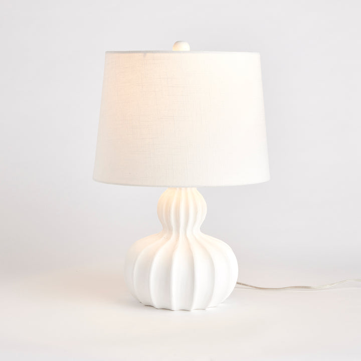White mango wood table lamp softly lit to show warm glow through natural jute cotton shade and carved base detail
