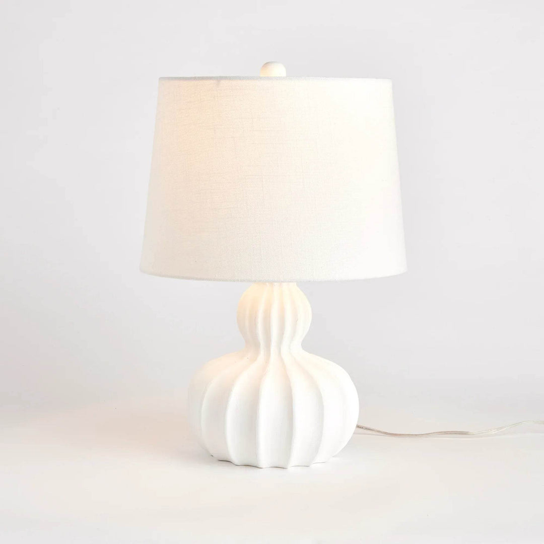 White mango wood table lamp softly lit to show warm glow through natural jute cotton shade and carved base detail
