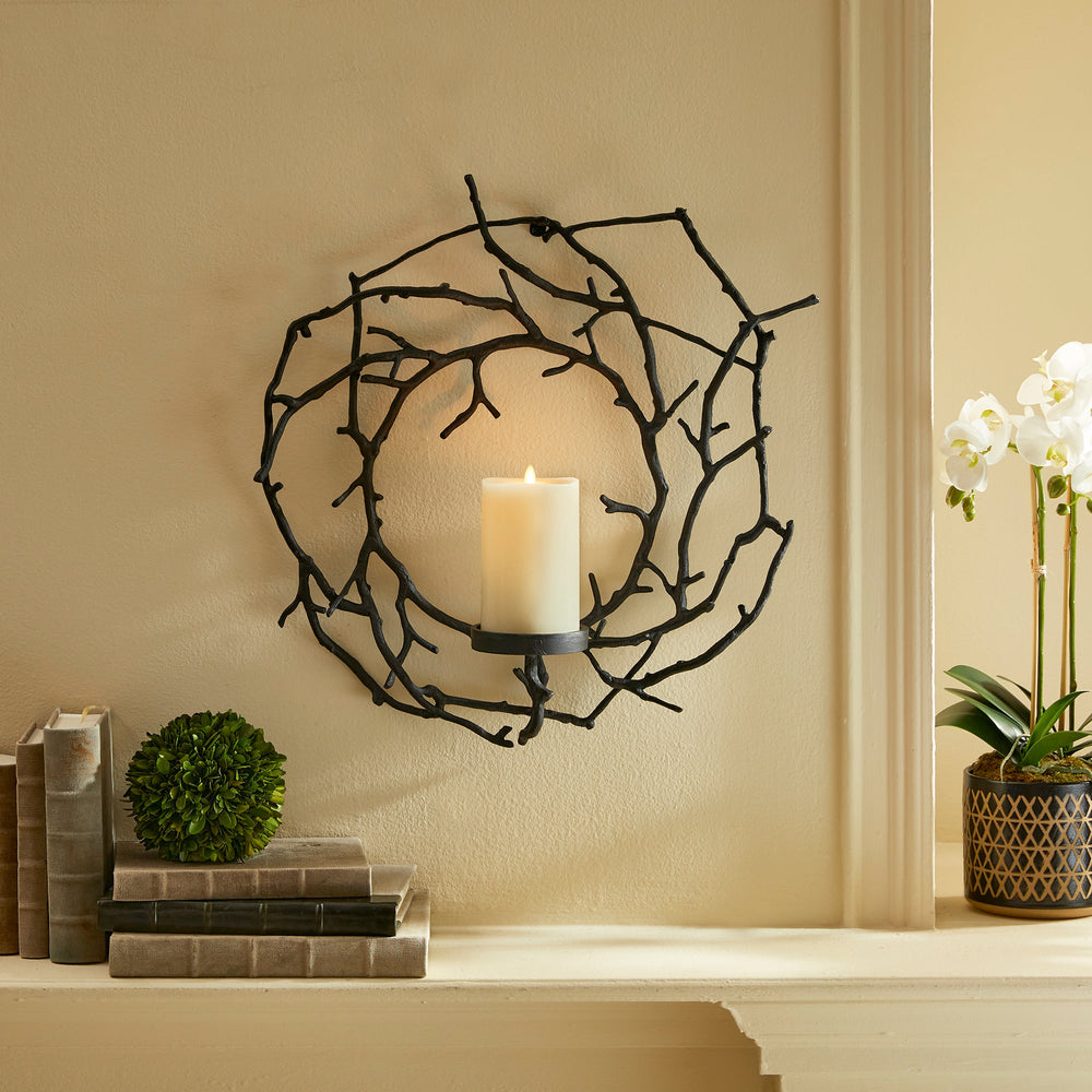 Sculptural black aluminum candle holder styled above a mantel in a rustic minimalist interior.

