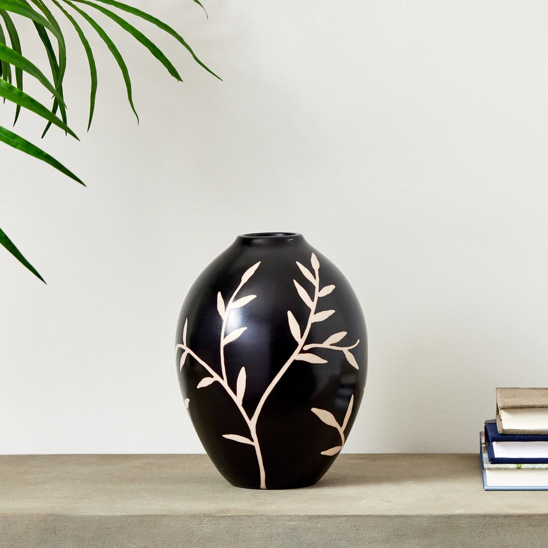 Medium black terracotta vase with etched vine pattern on console next to stacked books – Modern Organic.