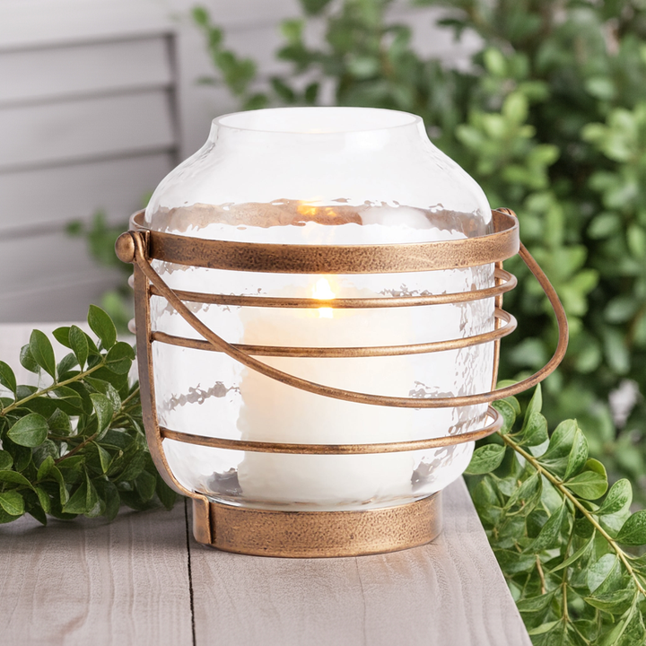 Hammered glass hurricane with antique gold iron banding, styled outdoors on stone surface with pillar candle – Coastal