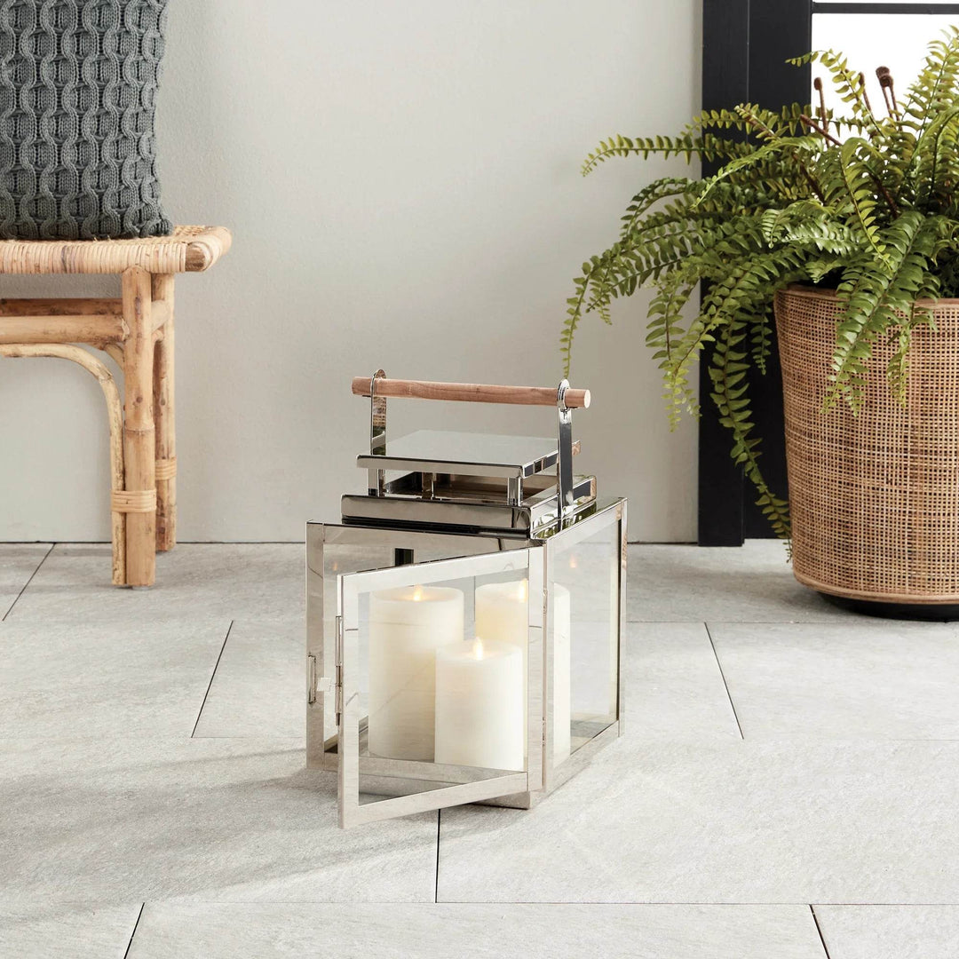 Medium silver outdoor lantern with teak handle styled beside a rattan bench and potted fern