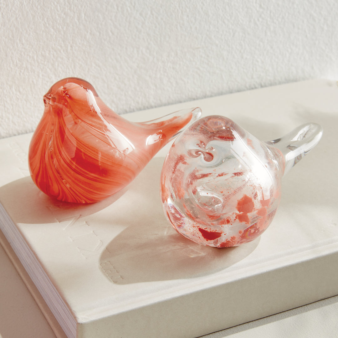 Hand blown melon glass finch sculptures styled on books, small decorative bird accents adding color to interior décor.
