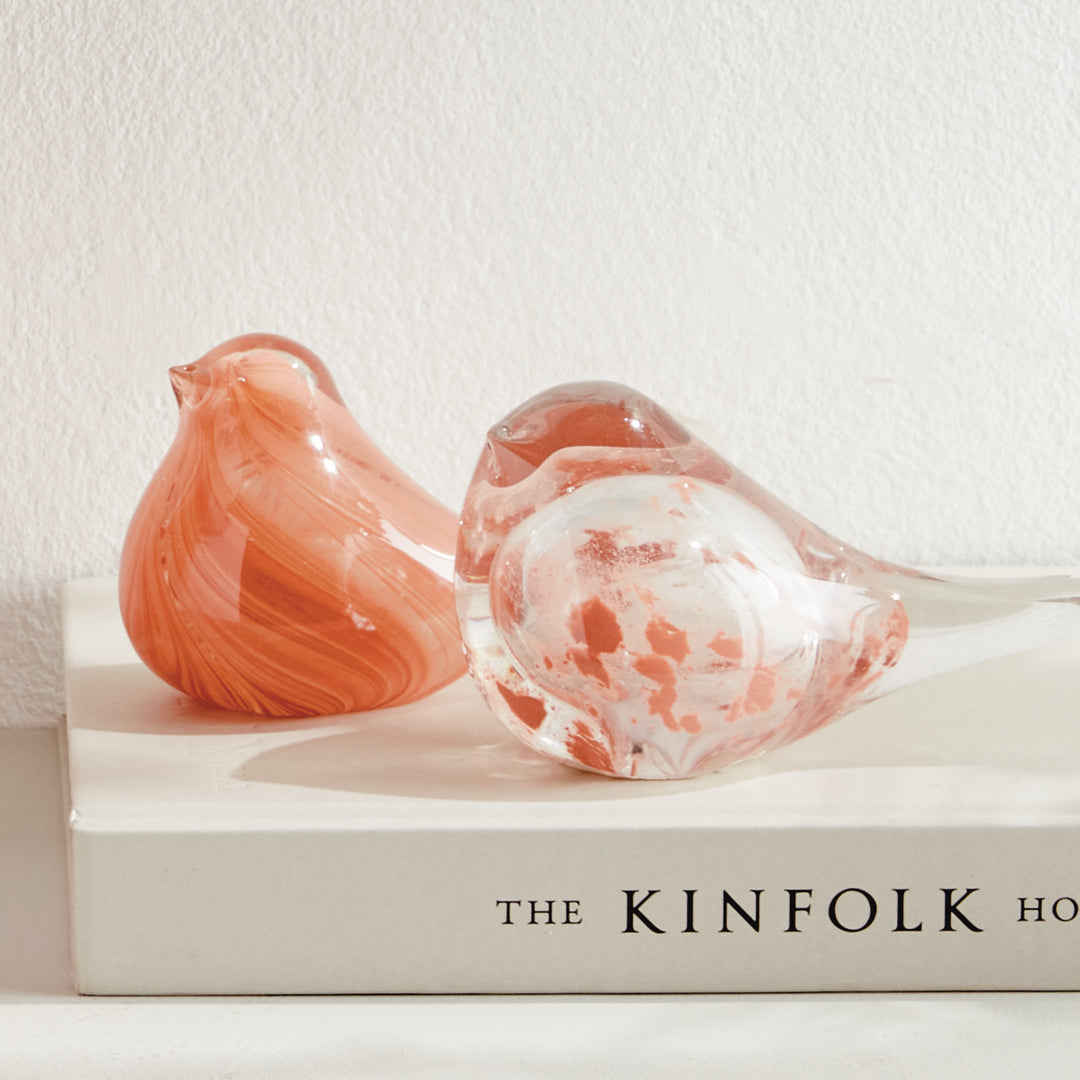 Set of two hand blown melon glass finch sculptures styled on stacked books, decorative bird accents for shelves.