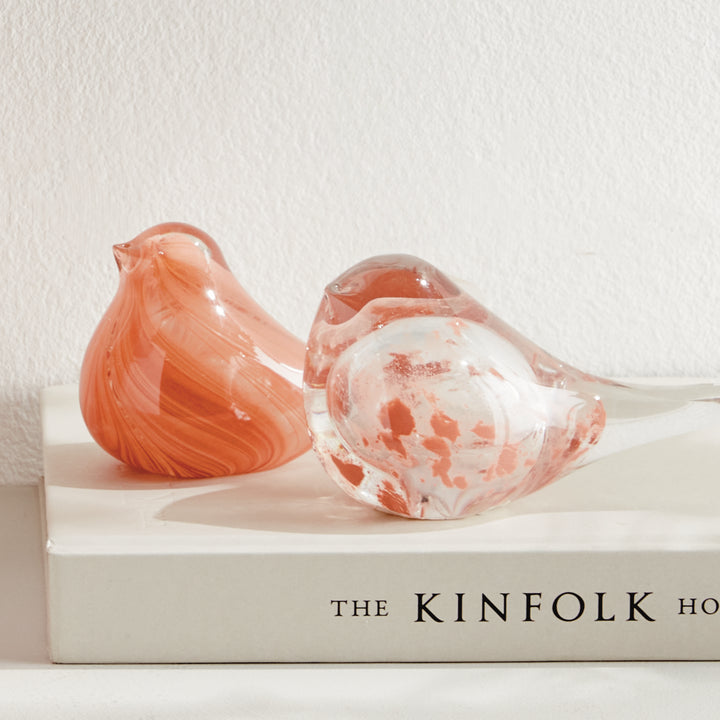 Set of two hand blown melon glass finch sculptures styled on stacked books, decorative bird accents for shelves.