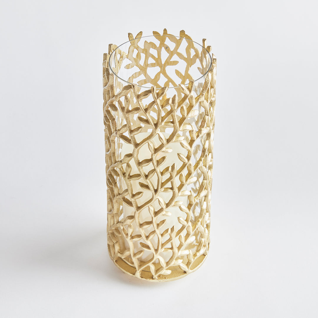 Cutout metal hurricane lantern in matte gold with leaf motif, perfect for modern botanical and nature-inspired decor themes.

