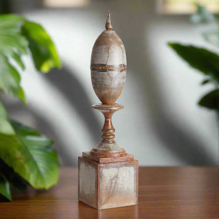 Rustic industrial metal finial decor shown on a tabletop with leafy indoor plants and soft directional lighting.
