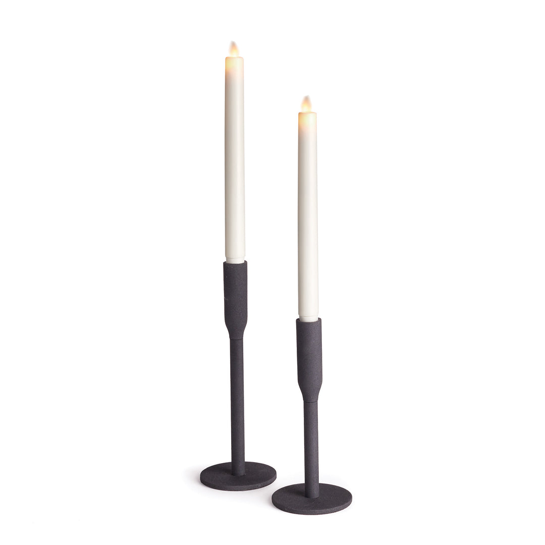 Pair of matte black metal taper candle holders in two heights, with round bases and white LED tapers shown - Transitional