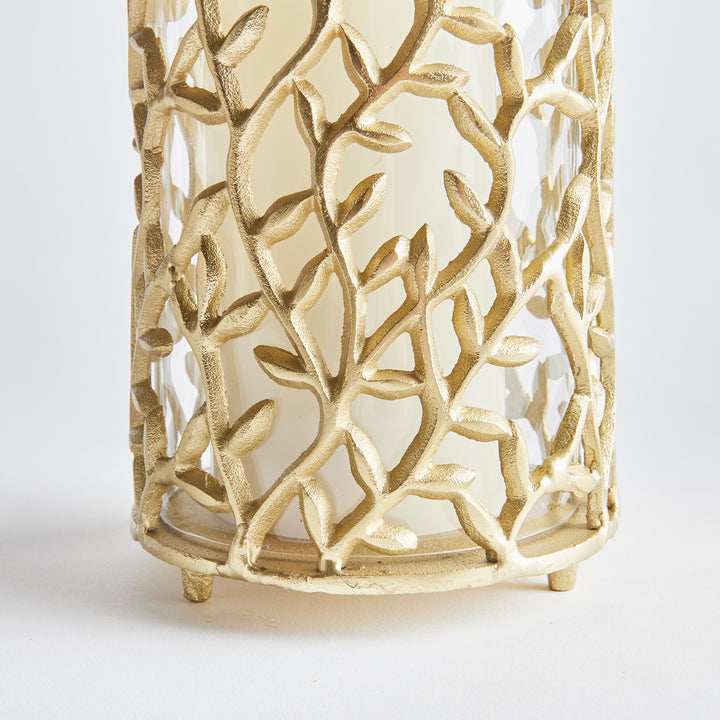 Modern botanical hurricane candle holder featuring gold vine frame and inner glass cylinder for ambient tabletop glow.

