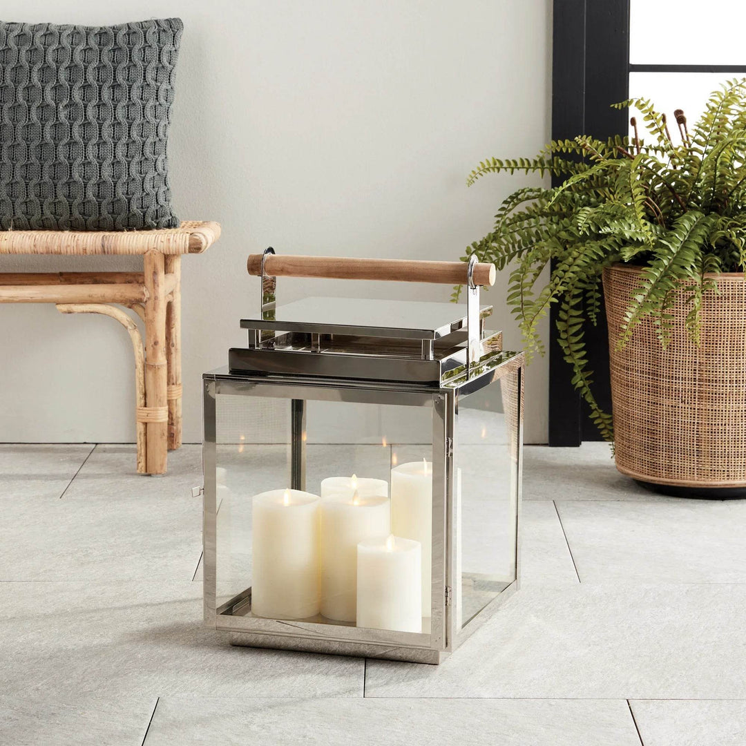 Modern coastal outdoor lantern styled on patio with candles and greenery.