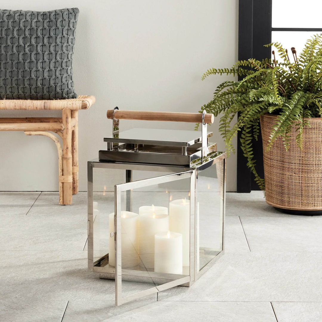 Modern coastal outdoor lantern placed by rattan bench and potted fern.