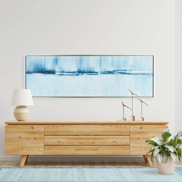 Horizontal wall art with oceanic palette displayed above wood console, styled in a coastal living room.

