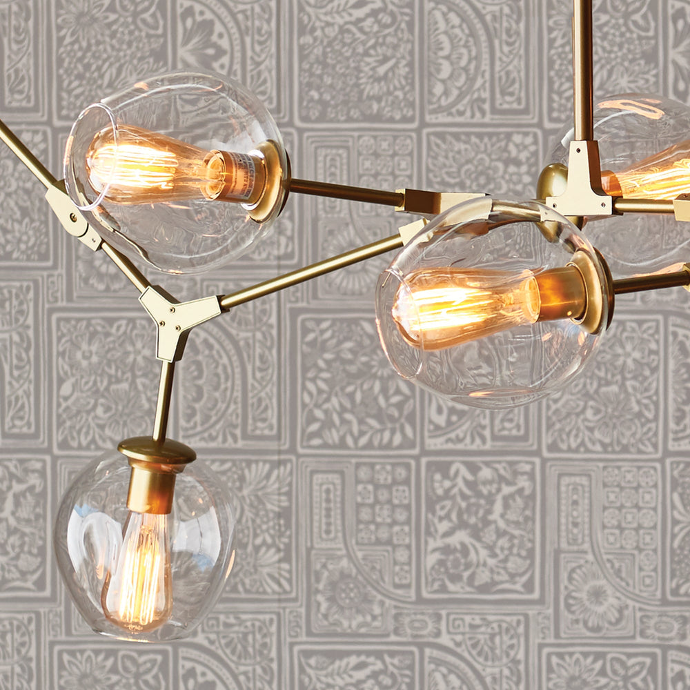 Close-up view of brass chandelier arm with exposed joints and clear glass globe encasing filament bulb.
