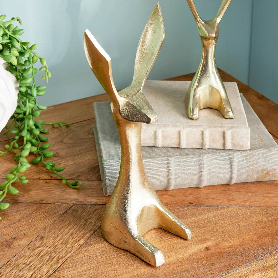 Gold aluminum rabbit sculptures displayed as decorative objects on tabletop with blue wall – Modern Coastal.