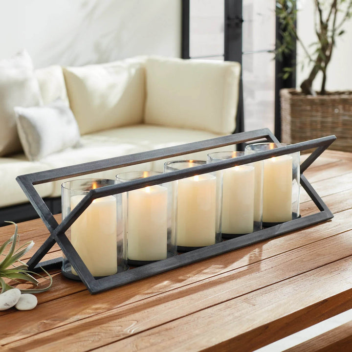 Black five-pillar candleholder with angular frame on outdoor wood table – Modern Industrial.