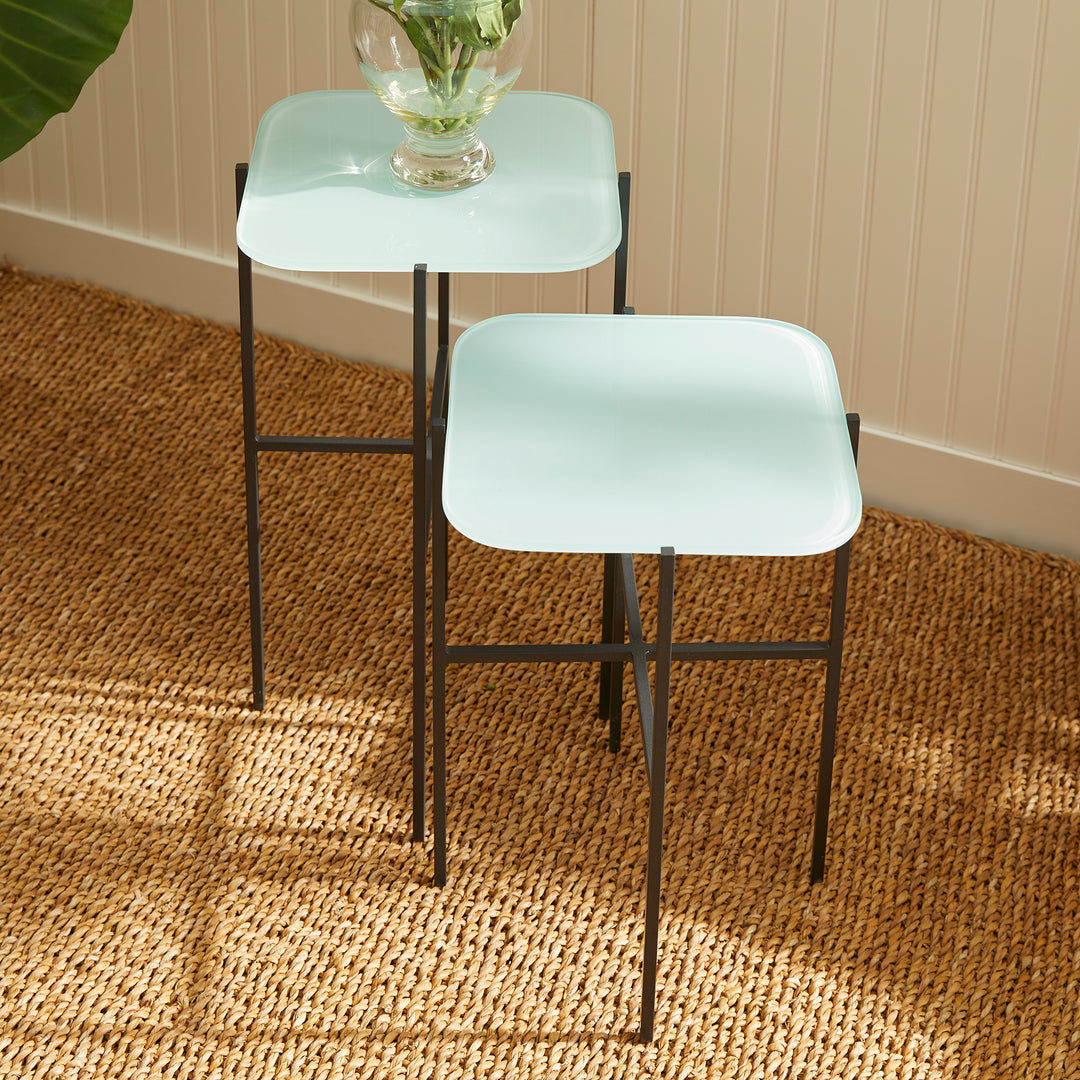 Blue glass side tables near plant and neutral-toned armchair in sunlit corner
