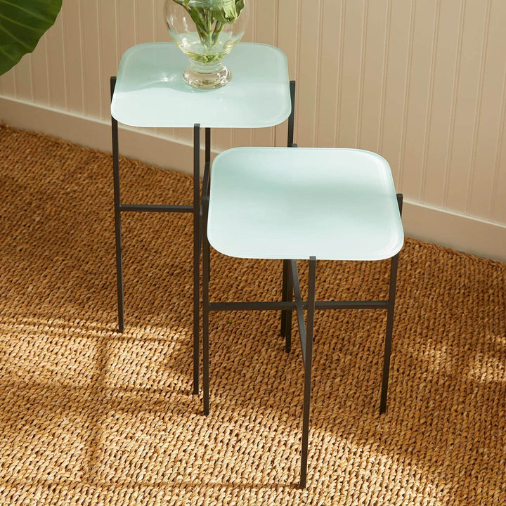 Blue glass side tables near plant and neutral-toned armchair in sunlit corner