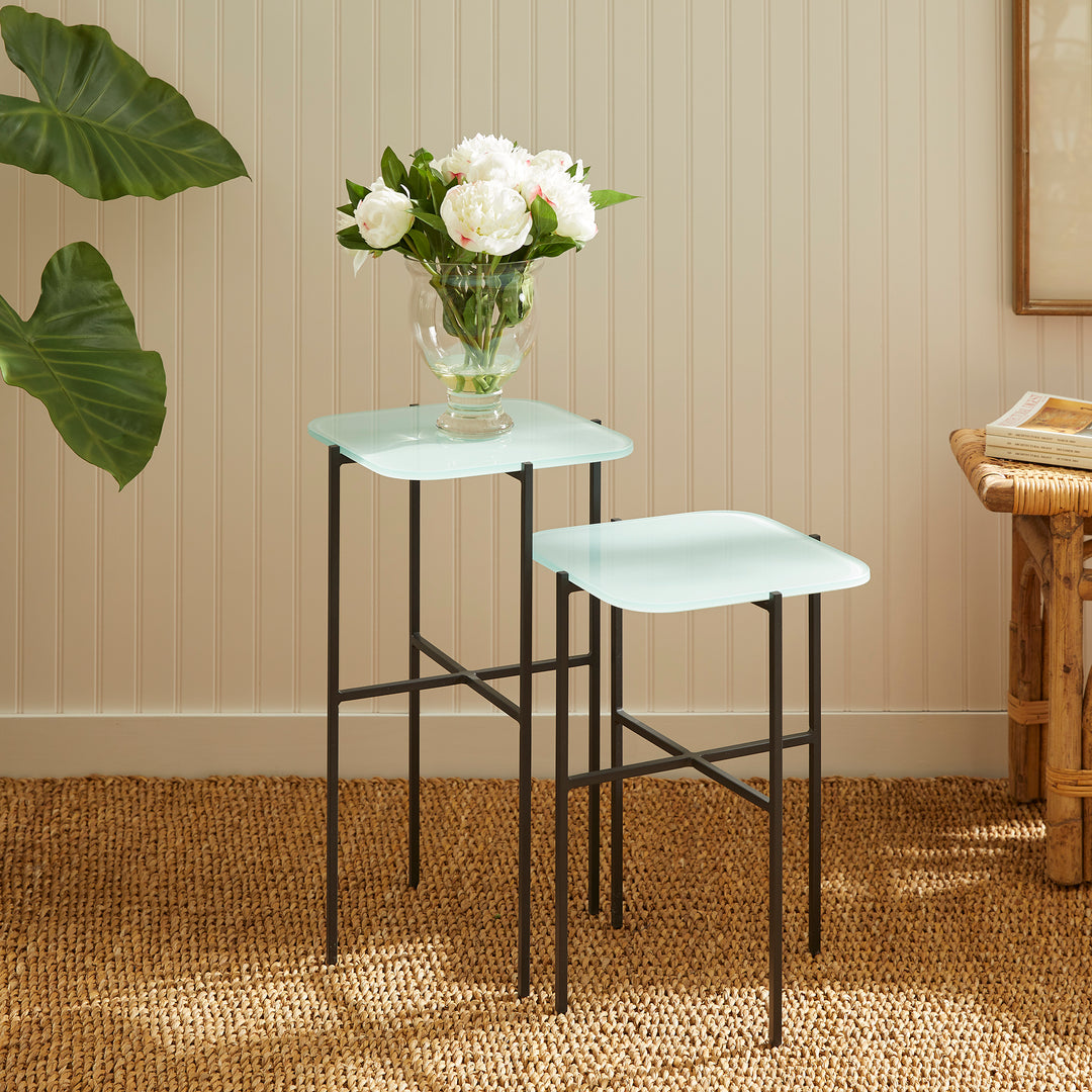 Blue glass side tables styled with flowers beside neutral wainscoting wall