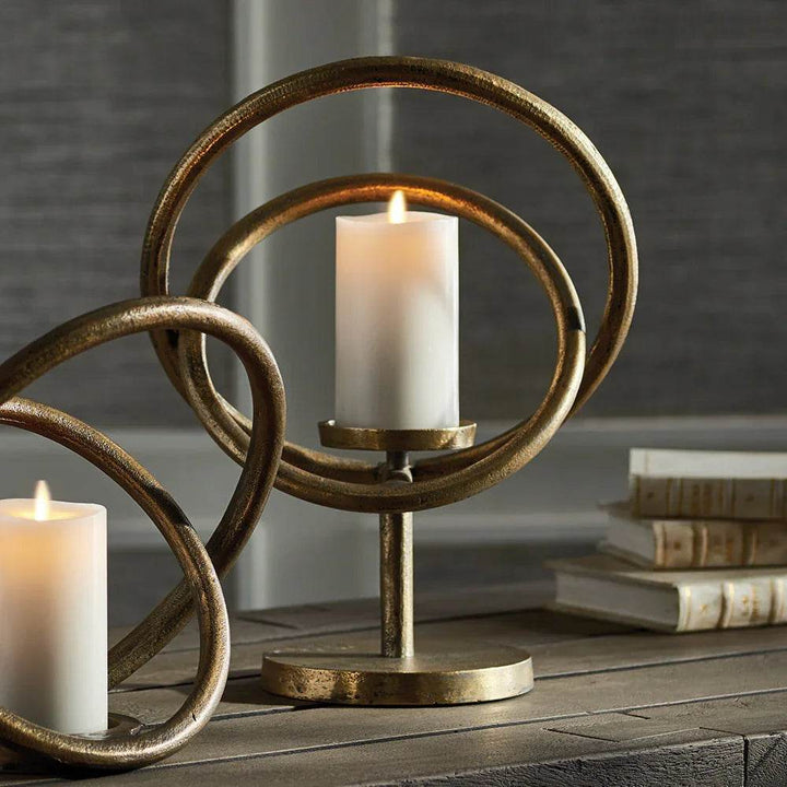 Orbit-style gold metal candle holder with LED pillar candle, styled with books on a dark wood table – Sculptural Modern

