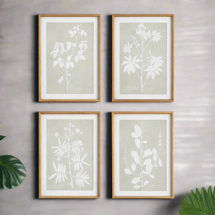 Modern organic framed botanical prints in taupe and white, styled against a soft gray wall with tropical leaf accents.