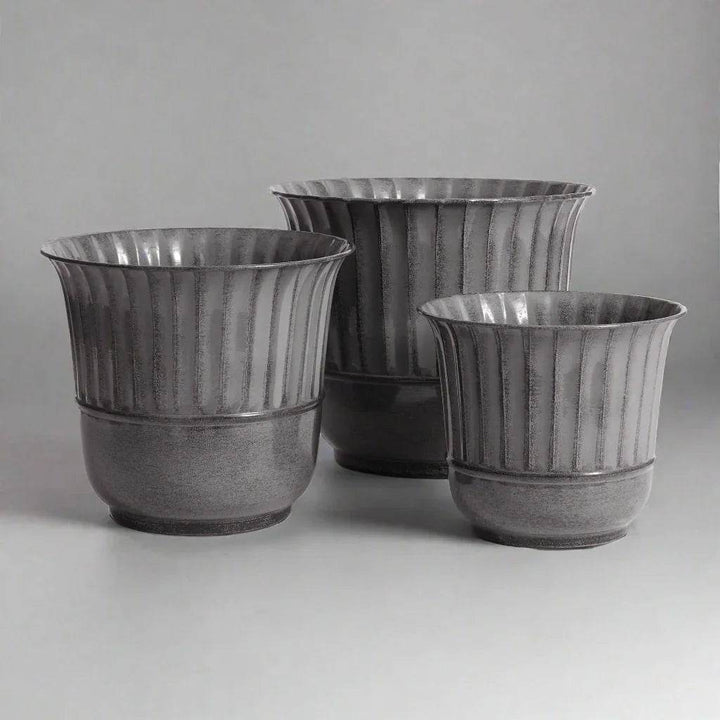 Set of three gray metal planters with vertical grooves shown at an angled indoor view