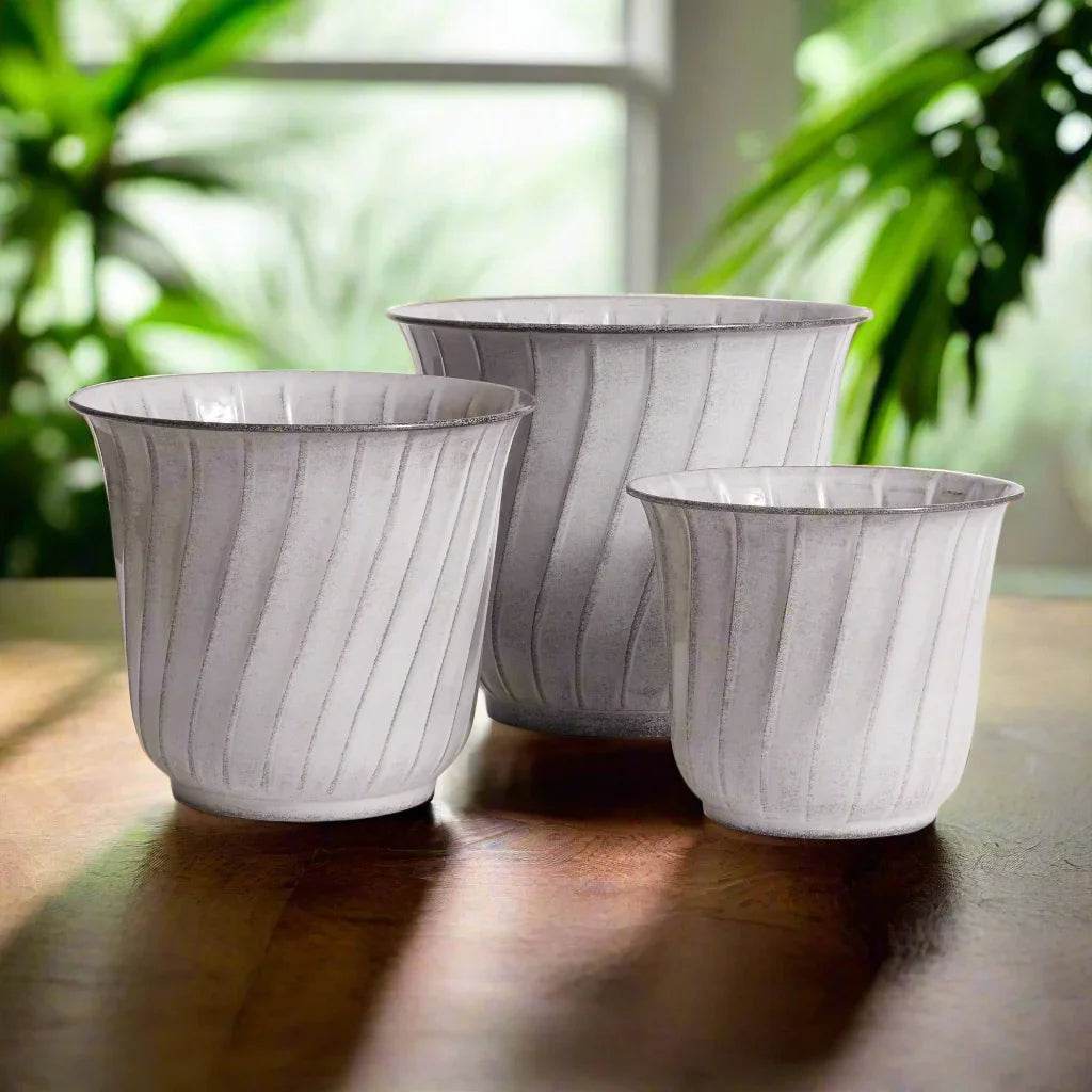 Set of modern organic white planters with soft vertical fluting styled in warm light interior with houseplants.