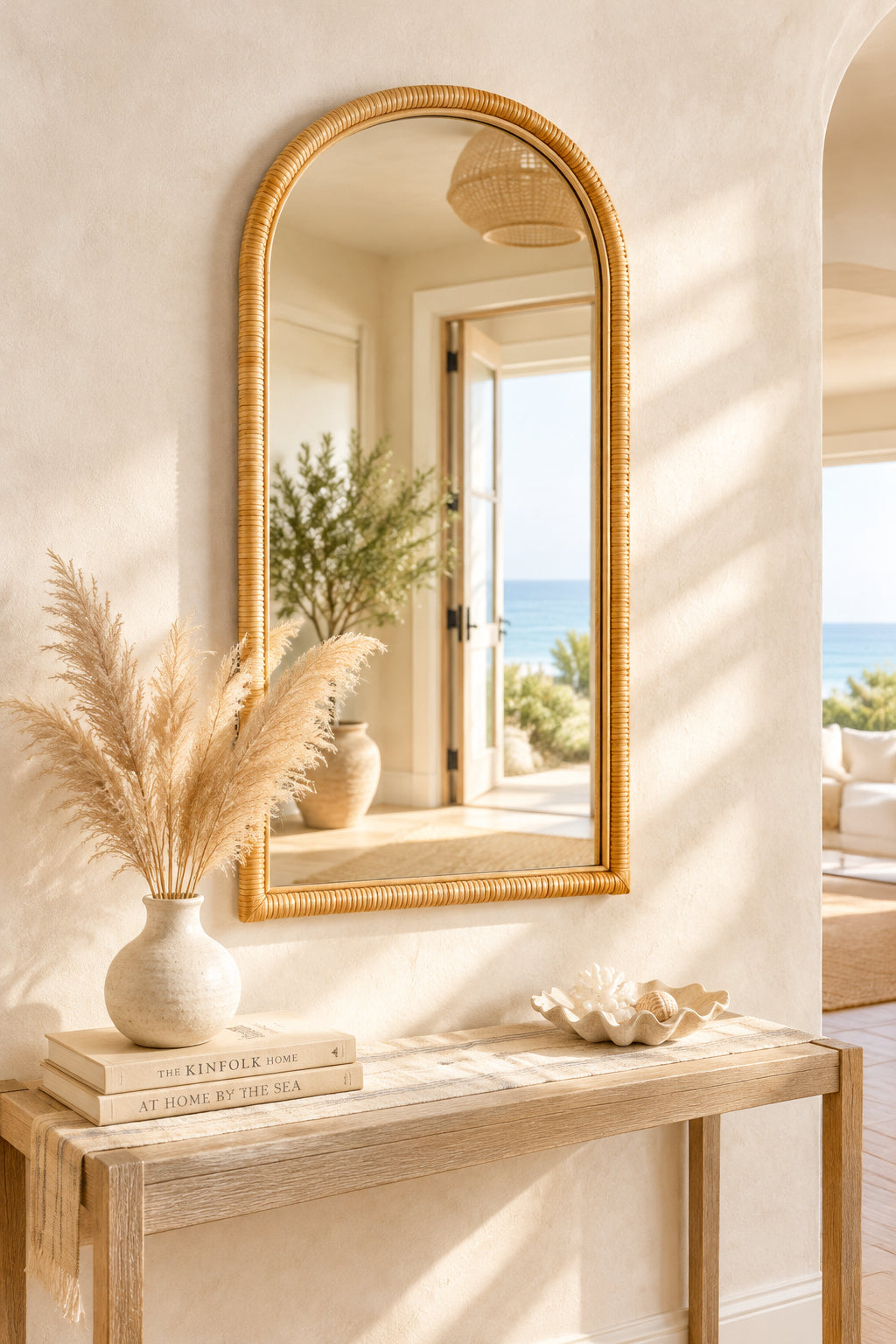 Natural rattan arched wall mirror above a light wood console with pampas grass and coastal decor in a sunlit entryway, Coastal