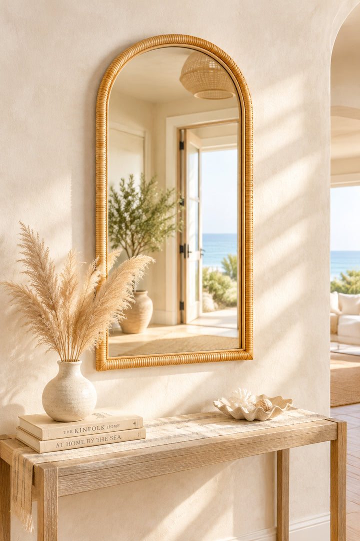 Natural rattan arched wall mirror above a light wood console with pampas grass and coastal decor in a sunlit entryway, Coastal