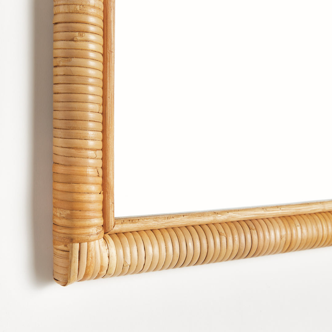 Close-up of natural rattan wrapped mirror frame showing ribbed texture and neatly joined lower corner in warm tan, Coastal