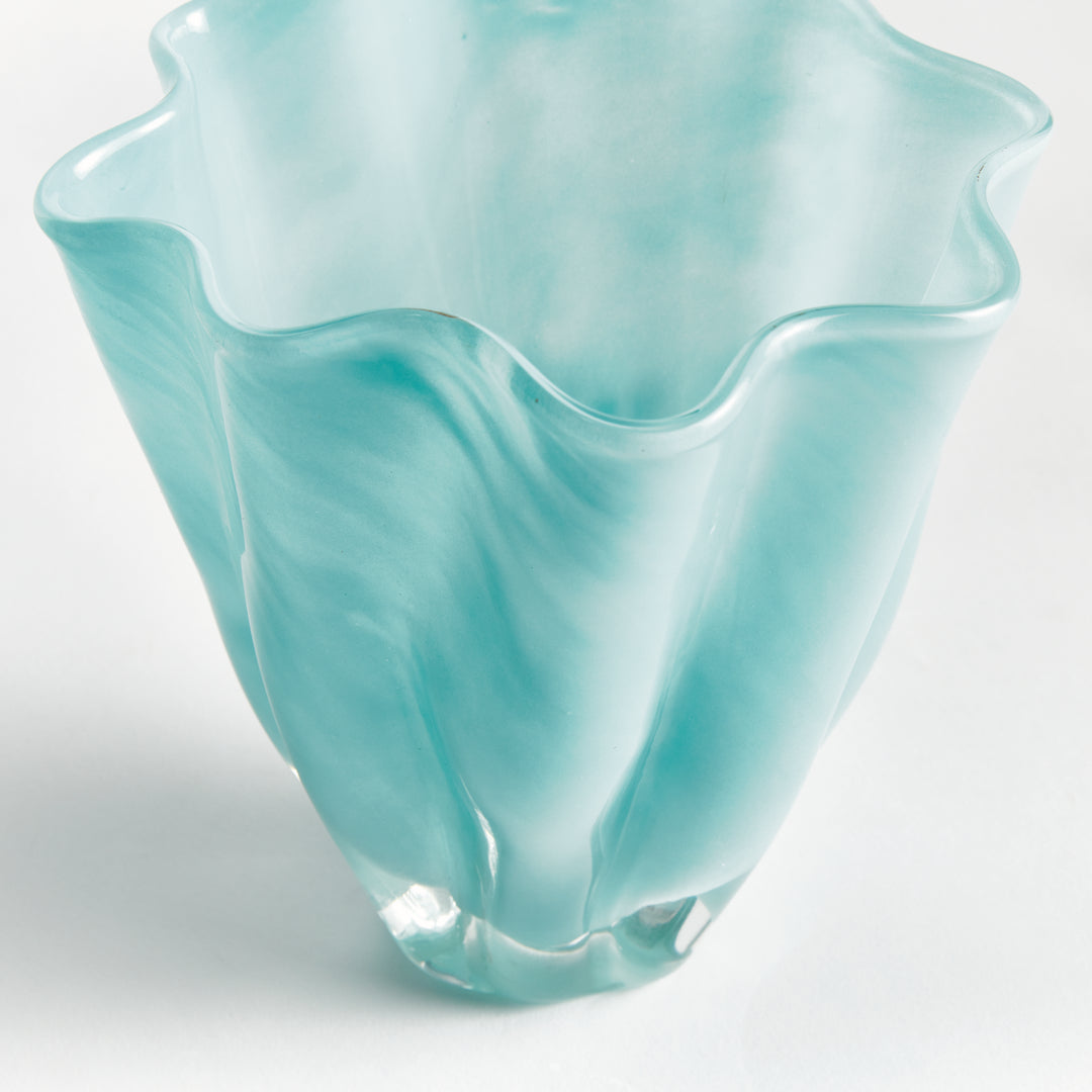 Close view of a light blue glass vase showing its undulating rim, tapered sides and flowing white color. Relaxed Coastal