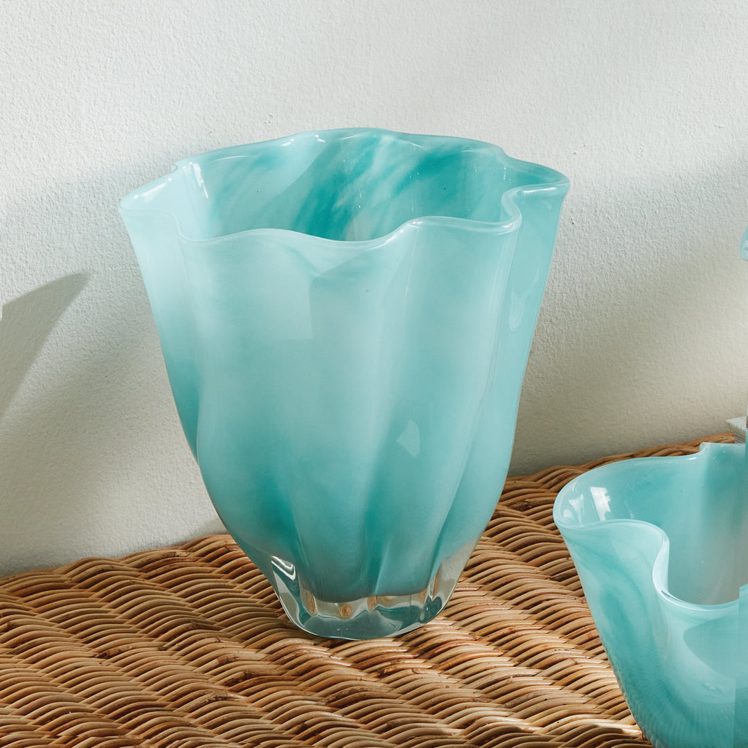Light blue glass vase styled on a woven table beside a coordinating bowl, showing the waved rim and base. Relaxed Coastal