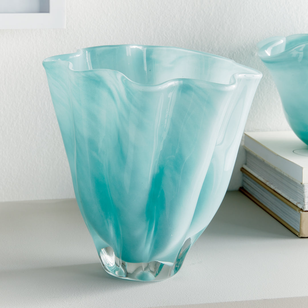 Light blue glass vase displayed beside books on a pale table, with a tall tapered body and softly waved rim. Relaxed Coastal