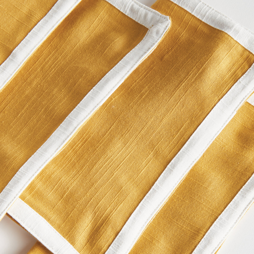 Close view of ochre woven cotton cocktail napkins with white borders, showing the fabric texture and edges, Transitional