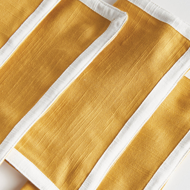 Close view of ochre woven cotton cocktail napkins with white borders, showing the fabric texture and edges, Transitional