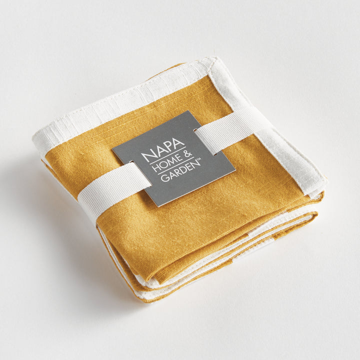 Four ochre cotton cocktail napkins with white borders, folded together and tied with a white ribbon on white, Transitional