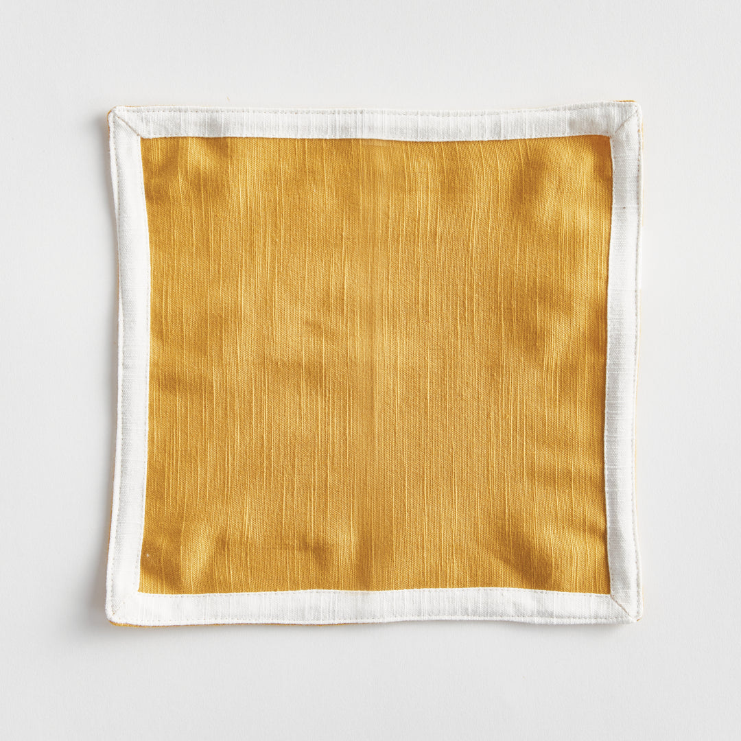 Ochre woven cotton cocktail napkin laid flat on a white background, showing its square shape and white border, Transitional