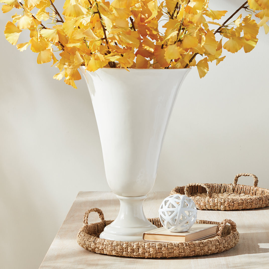 White trumpet pedestal vase holding yellow flowering branches, styled with a woven tray and white lattice orb | Traditional