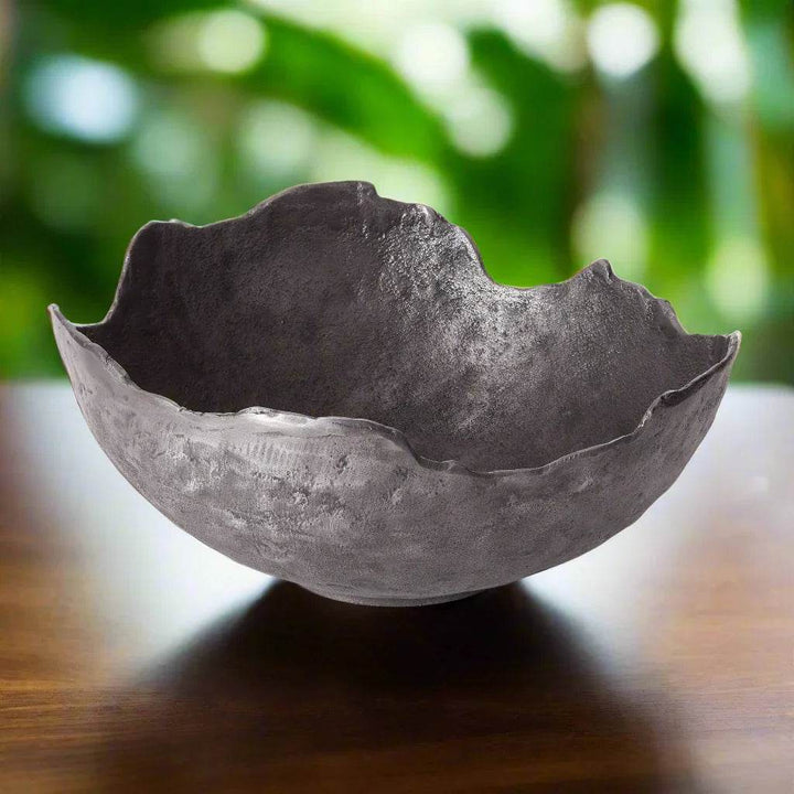 Artistic metal bowl in organic silhouette on wood surface, reflecting industrial luxe style for dining centerpieces