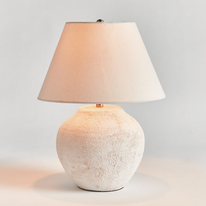 Orla white textured ceramic table lamp illuminated beneath a tapered linen shade on a plain light background. Modern Organic