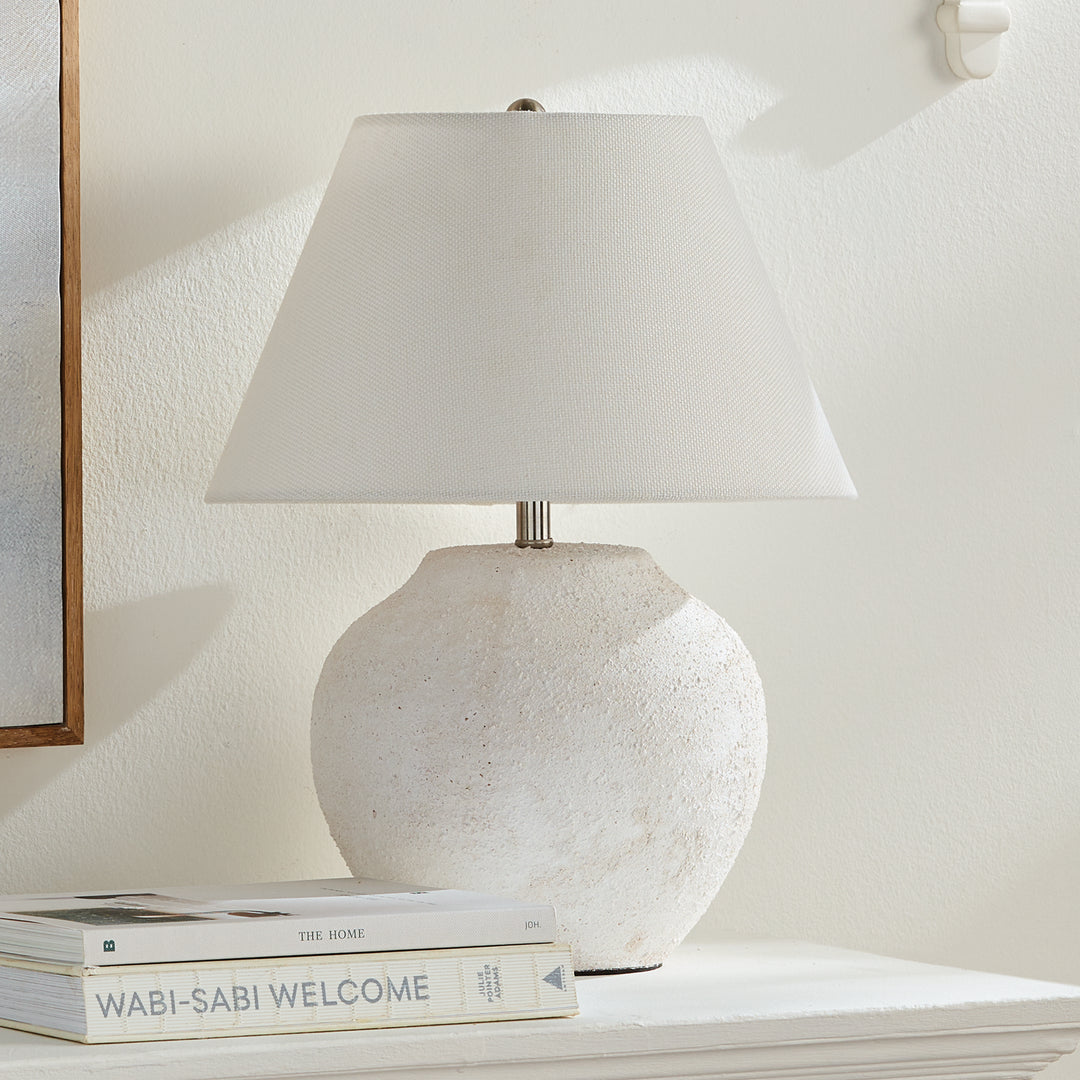Orla white textured ceramic table lamp with linen shade styled on a low table beside books and framed artwork. Modern Organic