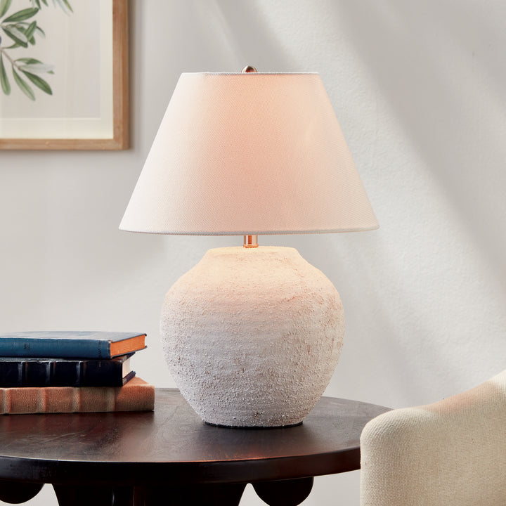Orla ceramic table lamp glowing beside stacked books on a dark wood table with an upholstered chair nearby. Modern Organic