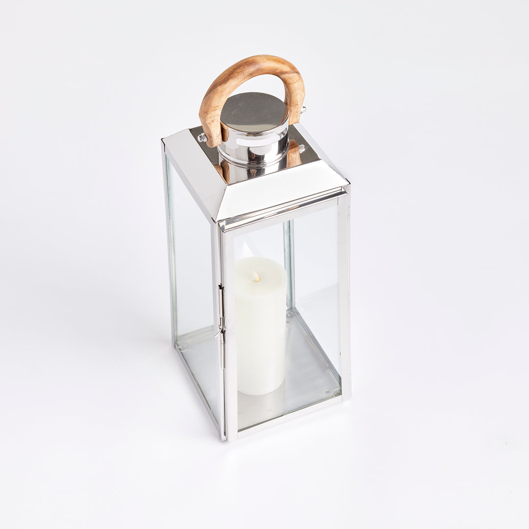 Small outdoor stainless steel lantern angled on white background with clear glass panels and teak handle coastal lantern