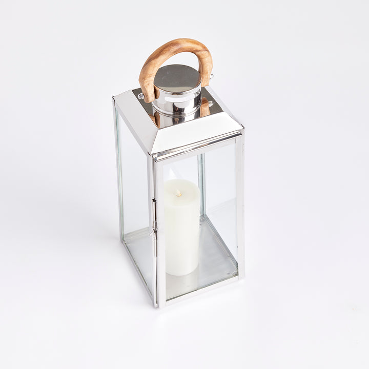 Small outdoor stainless steel lantern angled on white background with clear glass panels and teak handle coastal lantern