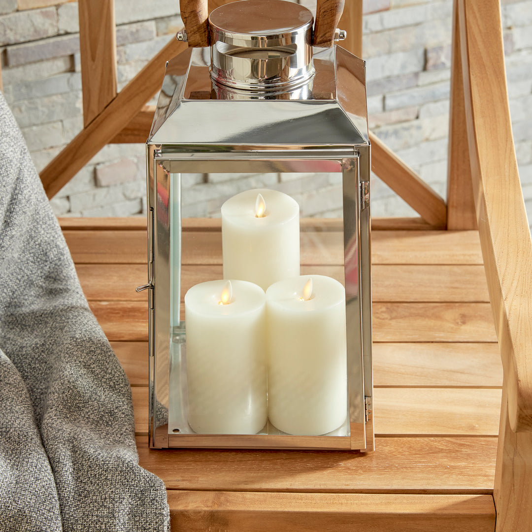 Small outdoor stainless steel lantern framed by wooden chair with candles on woven rug coastal lantern