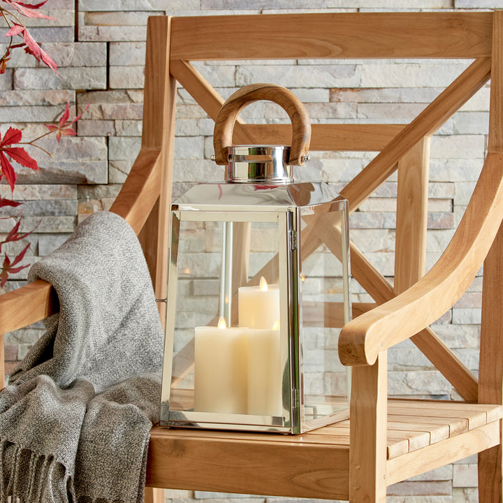 Small outdoor stainless steel lantern beside wooden chair with lit candles on woven rug coastal lantern