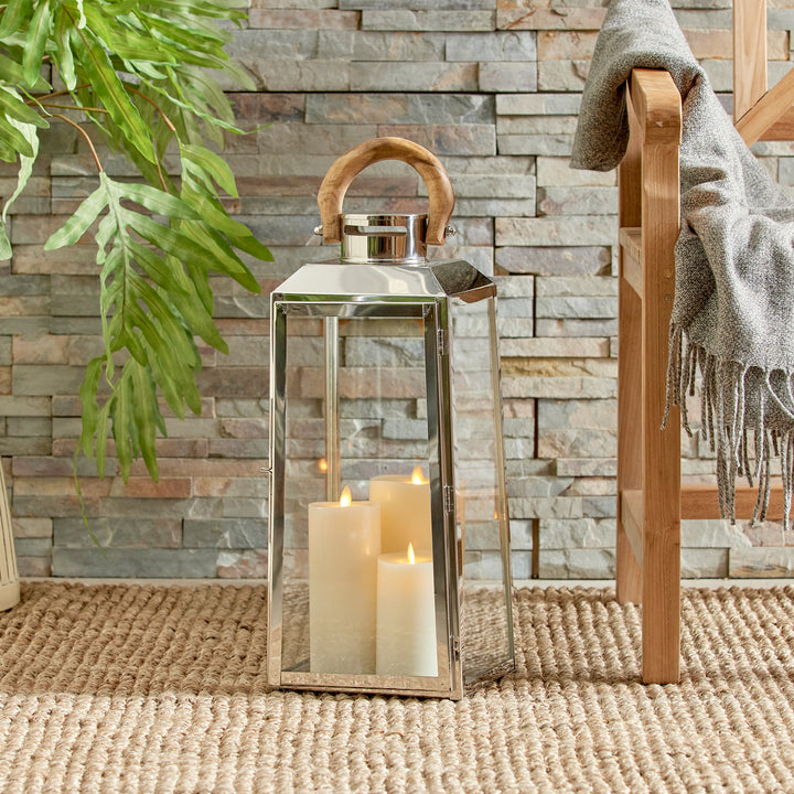 Small outdoor stainless steel lantern styled beside chair and plant on woven rug with candles coastal lantern