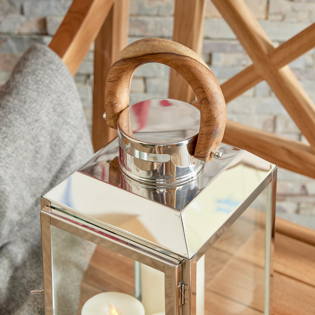 Small outdoor stainless steel lantern closeup styled on woven rug beside wood chair with candles coastal lantern