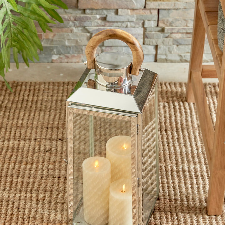 Small outdoor stainless steel lantern with candles styled on woven rug beside wood chair coastal lantern