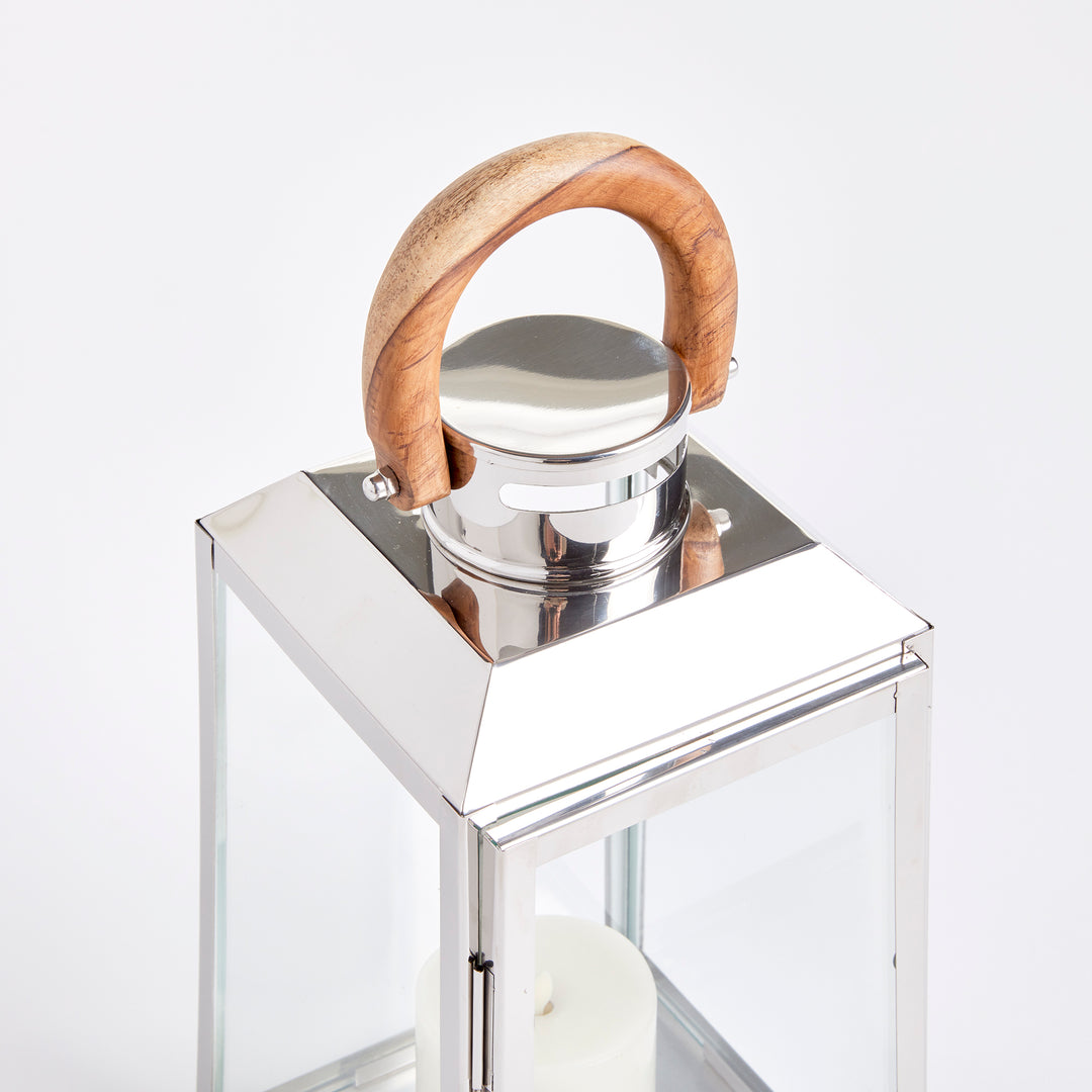 Small outdoor stainless steel lantern closeup showing teak wood handle and polished metal top on white coastal lantern