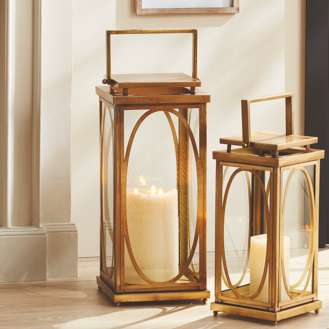 Brass oval frame candle lanterns styled on floor with warm ambient lighting for transitional interior décor lantern